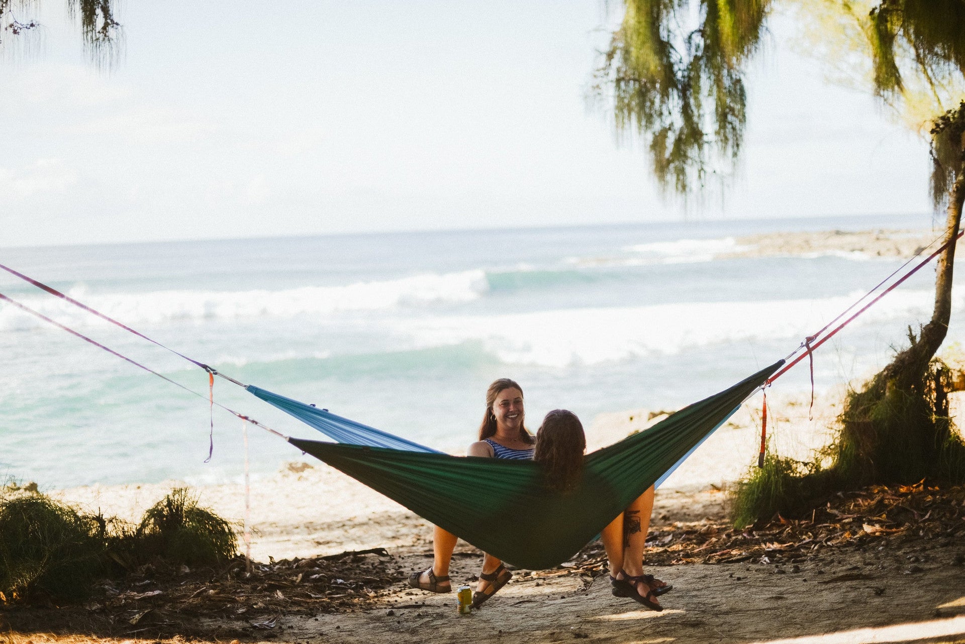 Two people sitting in a hammock suspended between two trees with Kammok Python Straps overlooking the ocean.