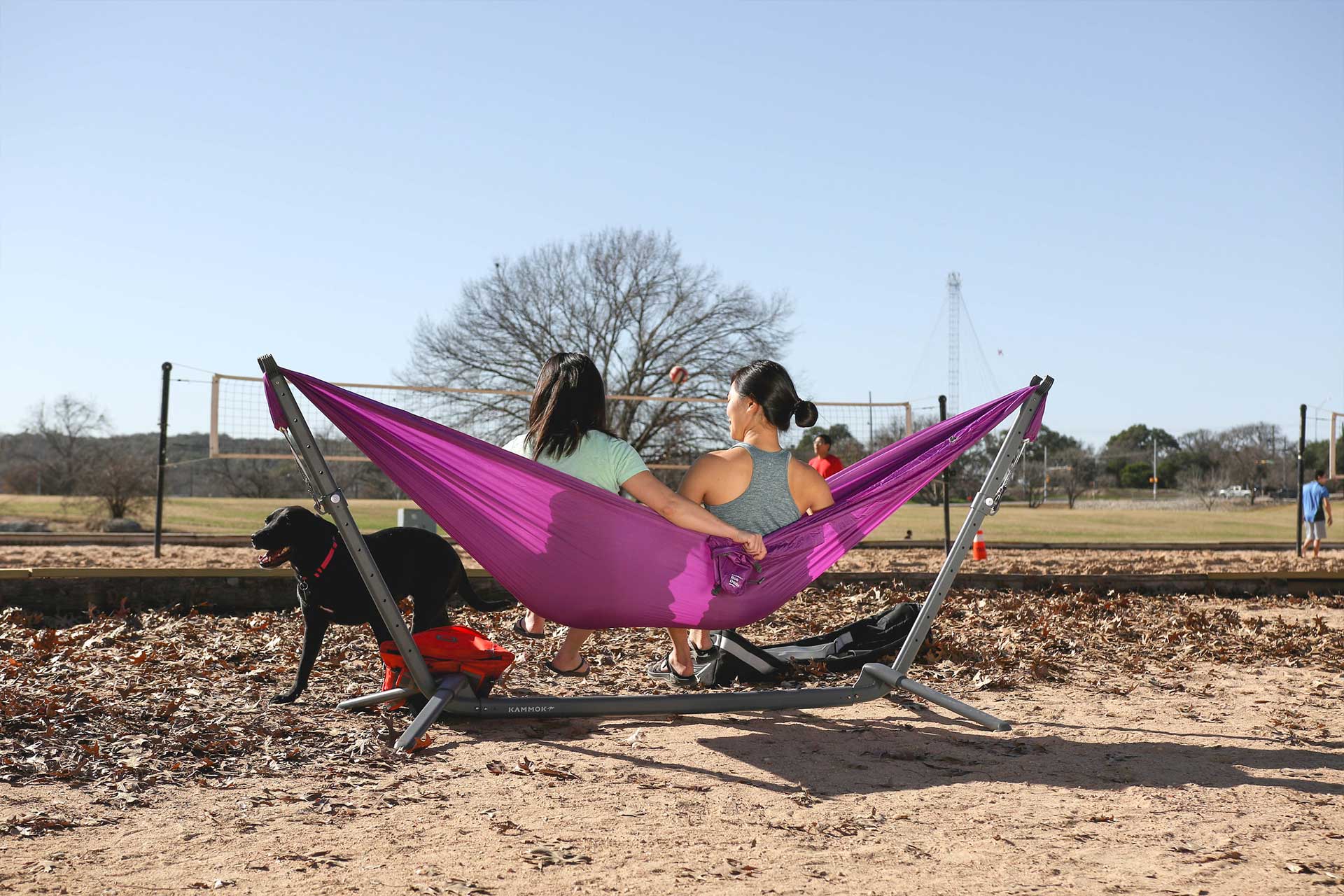 GIrls in a park overlooking a volleyball court sitting in a Swiftlet hammock stand.