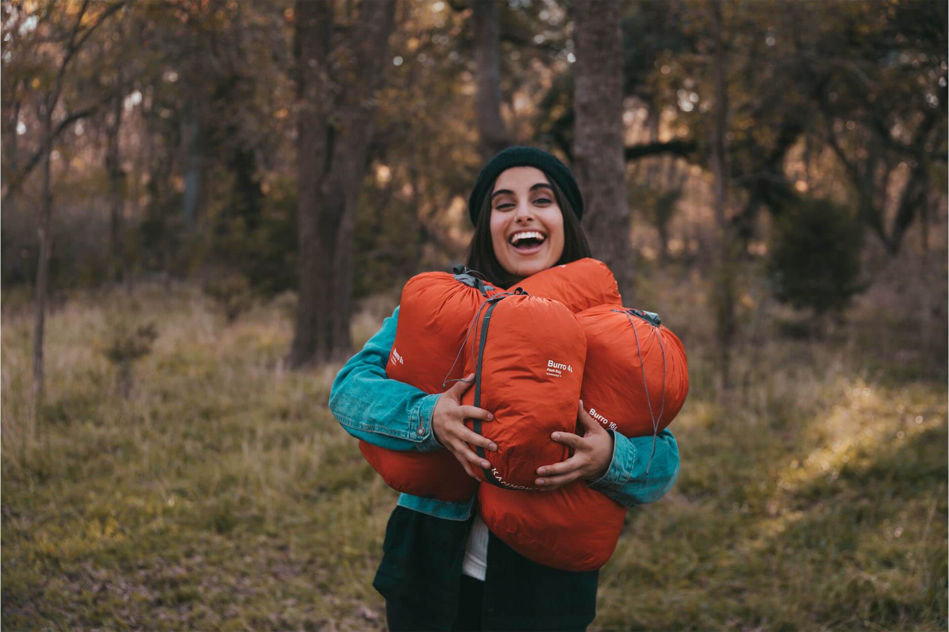 A women in the woods with her hands full of Kammok Blankets inside Burro Bags.