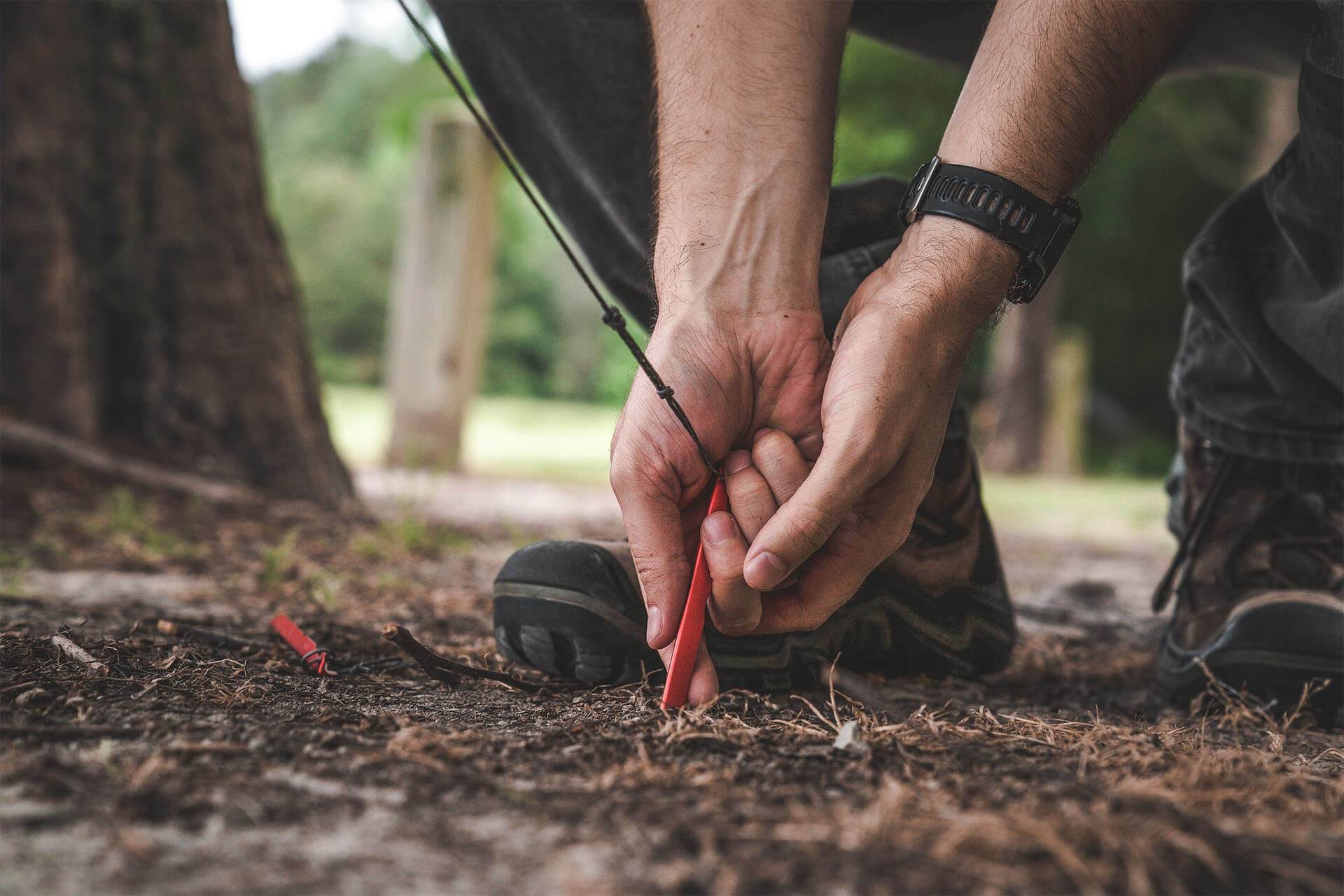 Man putting a stake in the ground for a shelter.