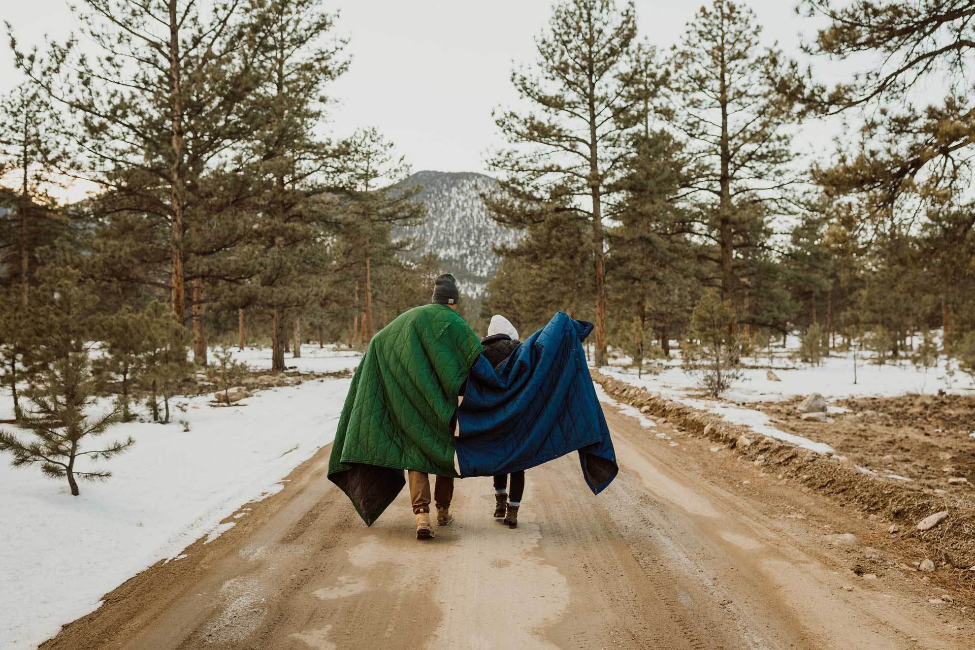 A couple walking down a dirt path with snow around them in Kammok Trail Quilts.